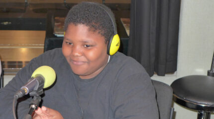 A youth wearing headphones sitting behind a microphone in a radio studio