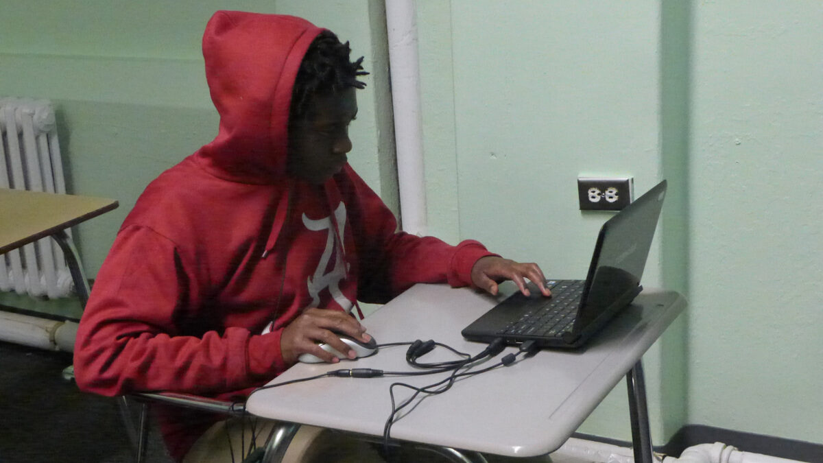 A teen interacting with a computer mouse and a laptop computer on a classroom desk