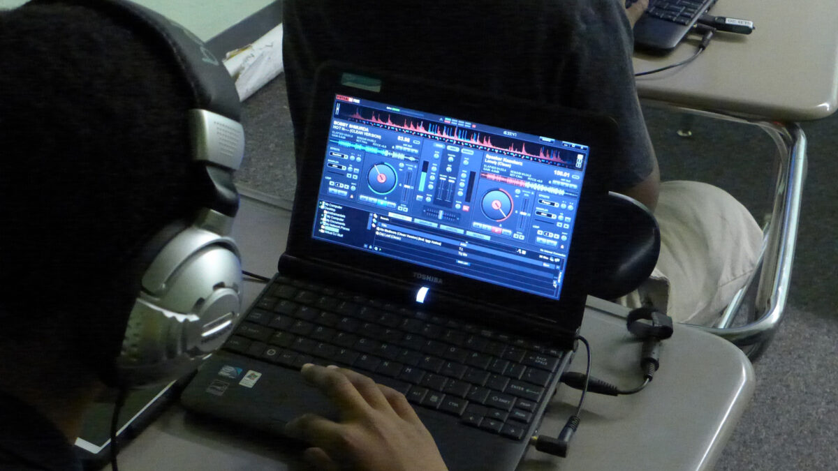 An individual wearing headphones looking audio mixing software on a laptop computer sitting at a classroom desk