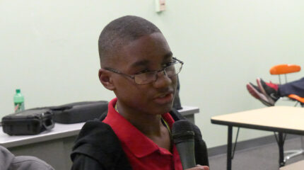 A youth holding and speaking into a microphone in a classroom