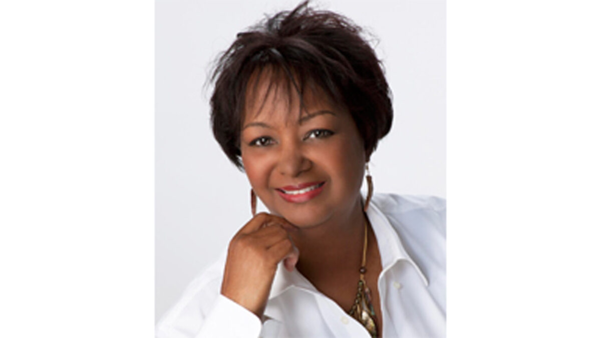 A headshot of an adult smiling and holding their hand up to their chin