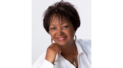 A headshot of an adult smiling and holding their hand up to their chin