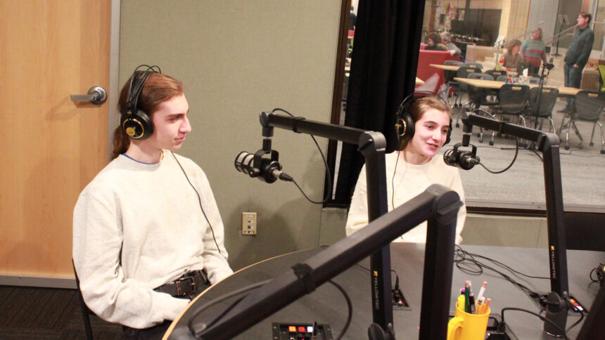Two teens wearing headphones speaking into microphones in a radio studio