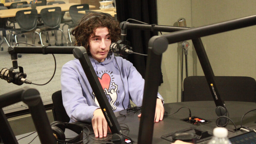 A teen wearing headphones speaking into a microphone in a radio studio