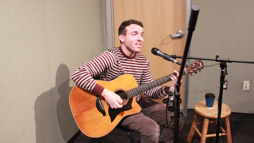 An adult playing an acoustic guitar and singing into a microphone in a radio studio