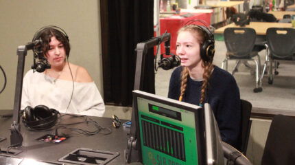 Two teens wearing headphones speaking into microphones in a radio studio