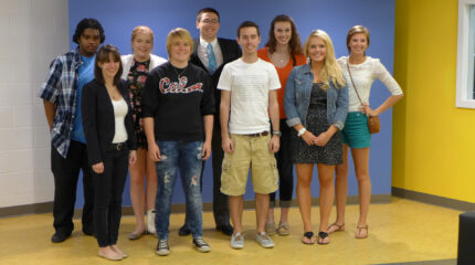 Nine adults smiling and standing in front of a blue wall