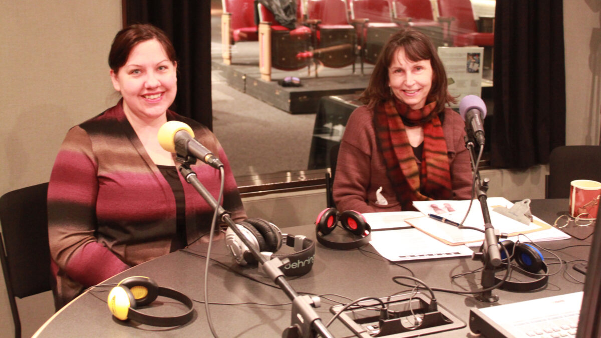 Two adults sitting behind microphones smiling at the camera in a radio studio