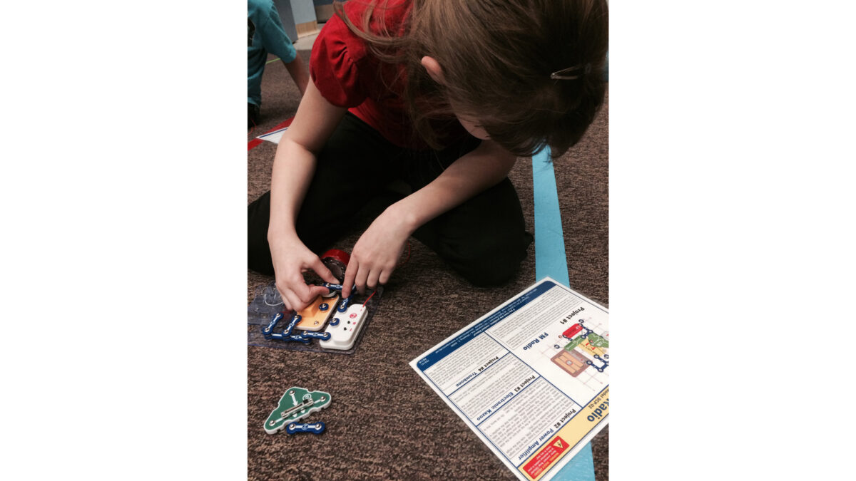 A youth looking down at instructions while building an electric contraption
