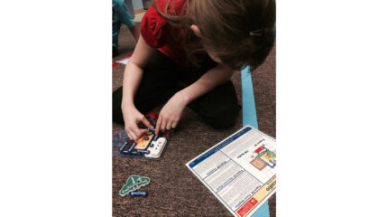 A youth looking down at instructions while building an electric contraption