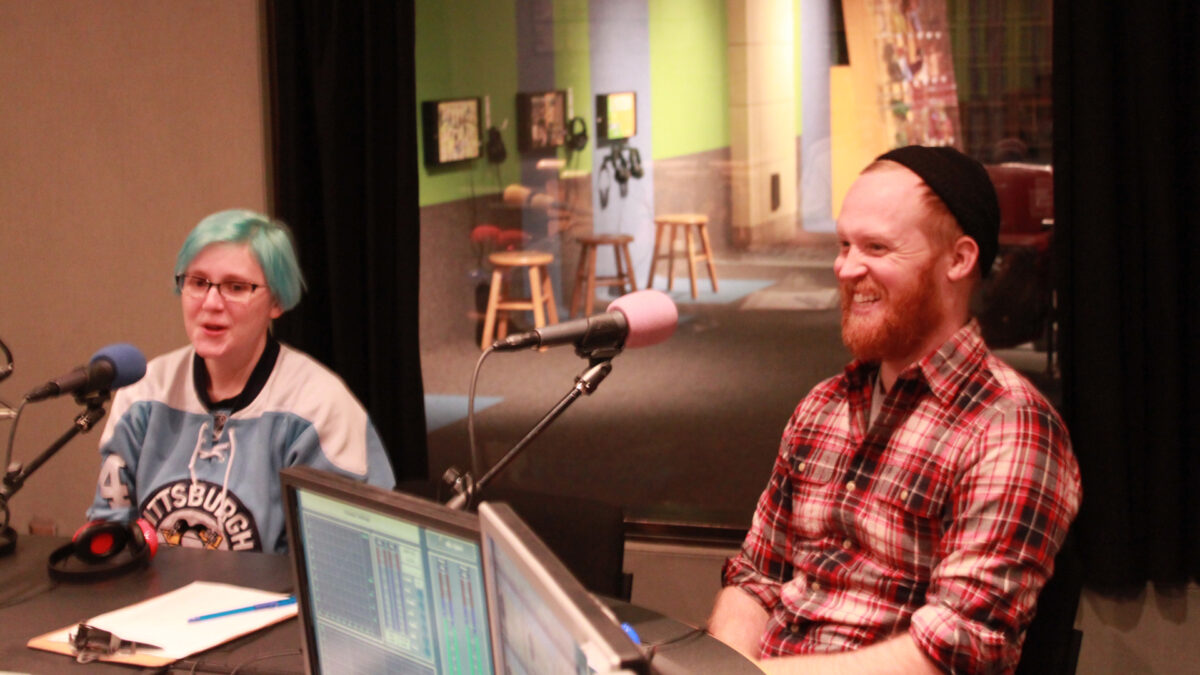 Two adults speaking into microphones in a radio studio