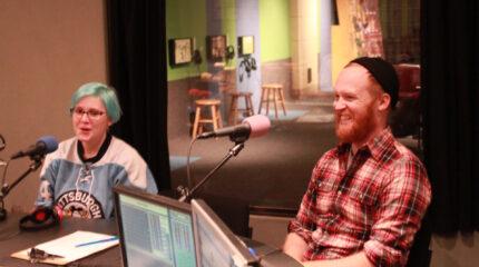 Two adults speaking into microphones in a radio studio