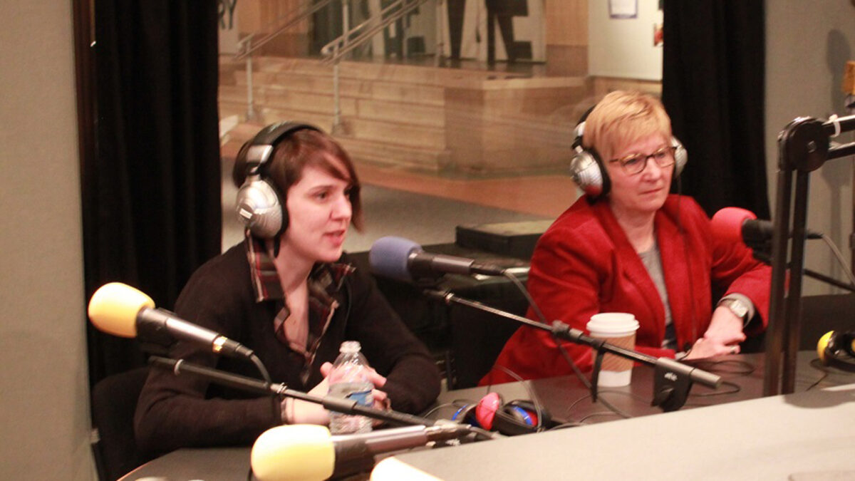 Two adults wearing headphones speaking into microphones in a radio studio
