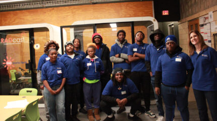 Eleven teens and one adult smiling and posing in profile in front of recording booths