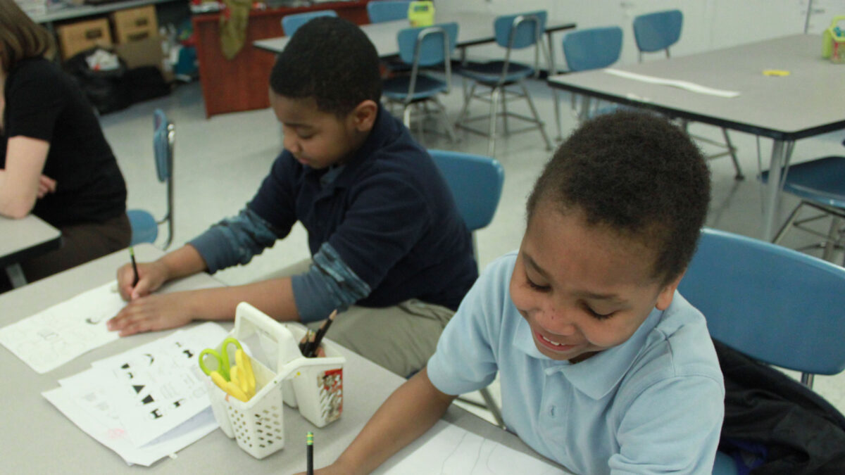 Two youth drawing on pieces of paper in a classroom
