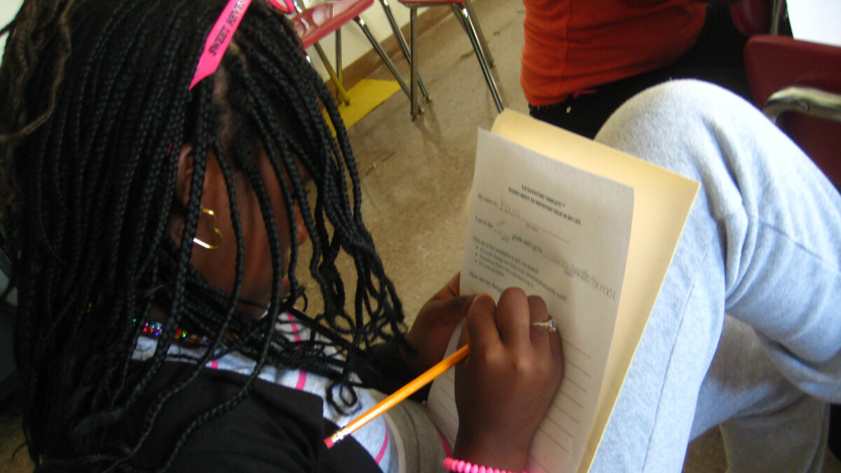 A youth writing on a piece of paper while sitting in a classroom