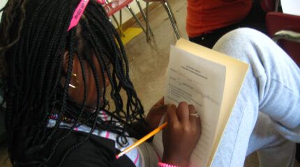 A youth writing on a piece of paper while sitting in a classroom