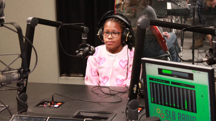 A youth wearing headphones sitting behind a microphone in a radio studio