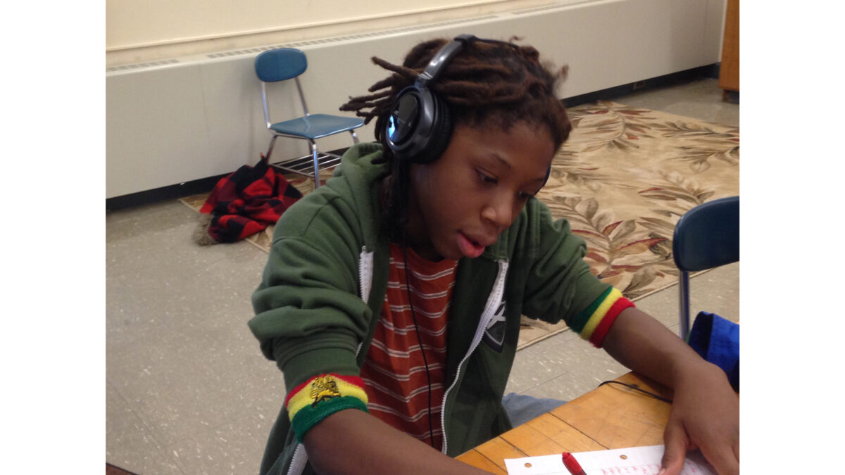 A youth wearing headphones looking down at a piece of paper on a classroom desk