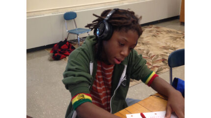 A youth wearing headphones looking down at a piece of paper on a classroom desk