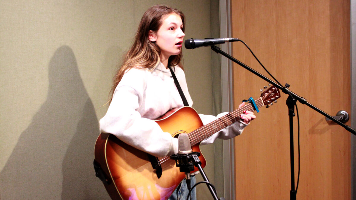 A teen playing acoustic guitar and singing into a microphone in a radio studio