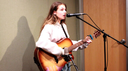A teen playing acoustic guitar and singing into a microphone in a radio studio