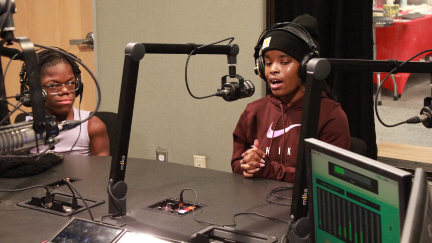 Two teens wearing headphones speaking into microphones in a radio studio