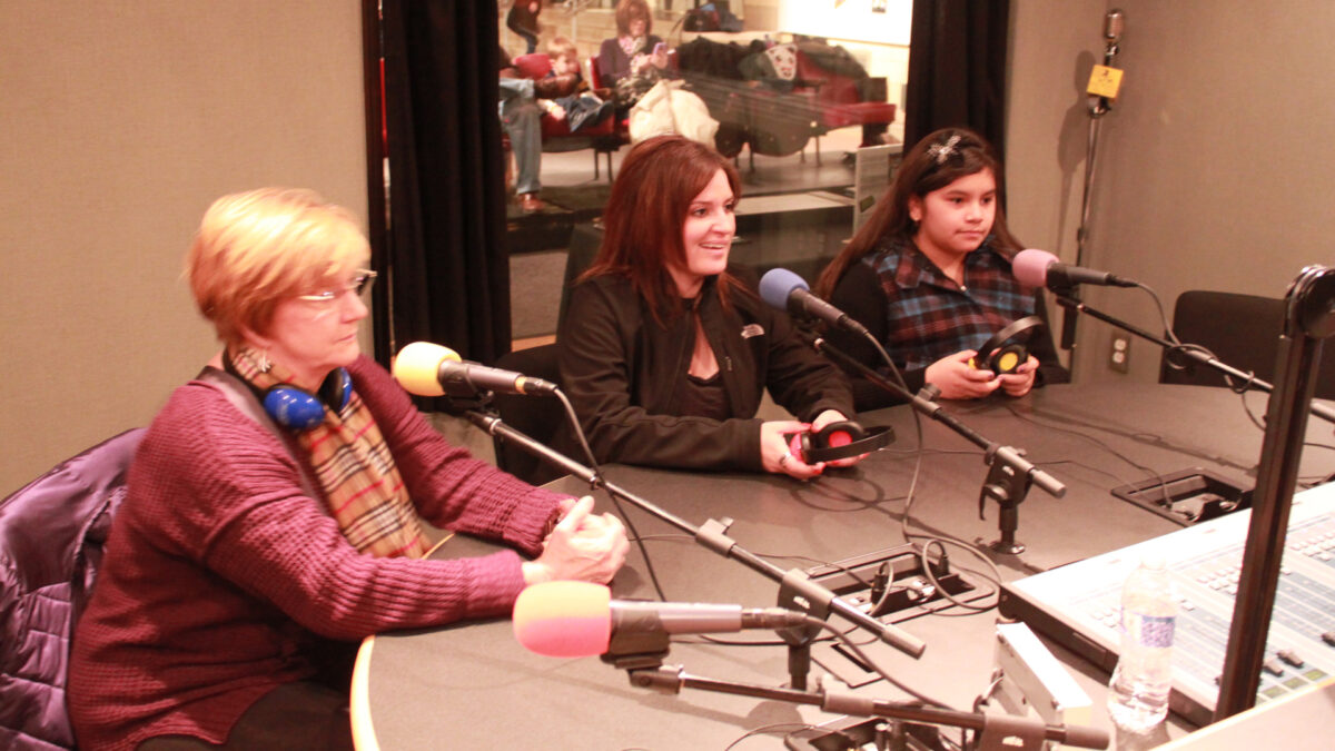 Two adults and a youth sitting behind microphones in a radio studio