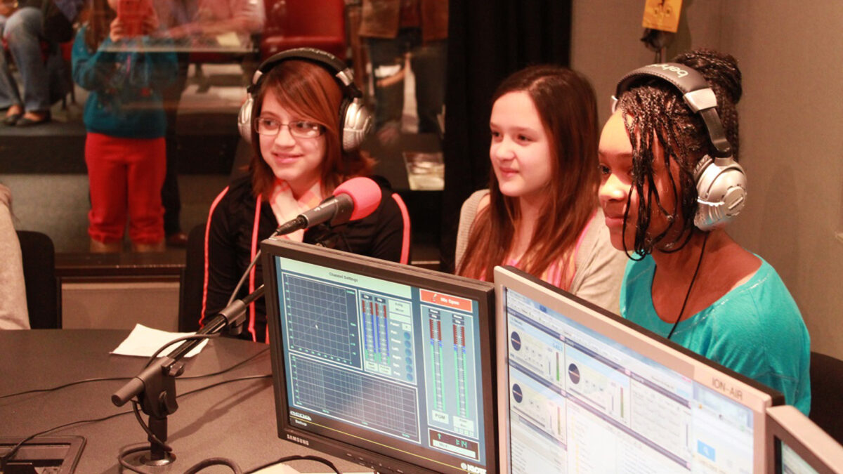 Three youth wearing headphones speaking into a microphone in a radio studio