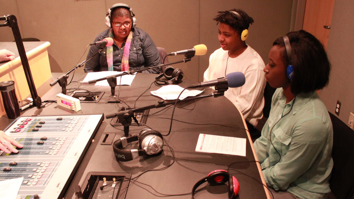 Three teens wearing headphones speaking into microphones in a radio studio