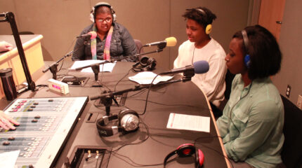 Three teens wearing headphones speaking into microphones in a radio studio