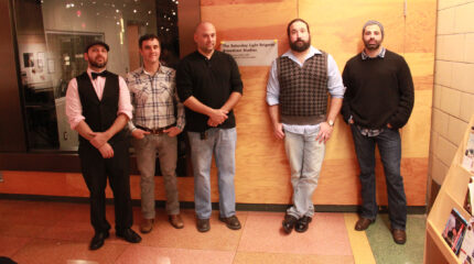 Five adults posing in front of a radio studio