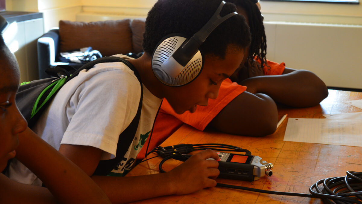 A youth wearing headphones looking at a portable recorder in a classroom