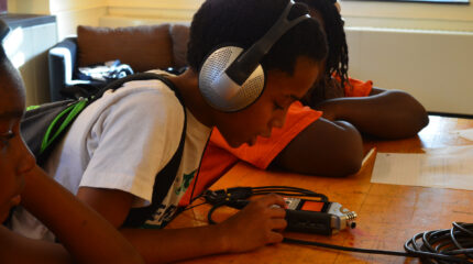 A youth wearing headphones looking at a portable recorder in a classroom