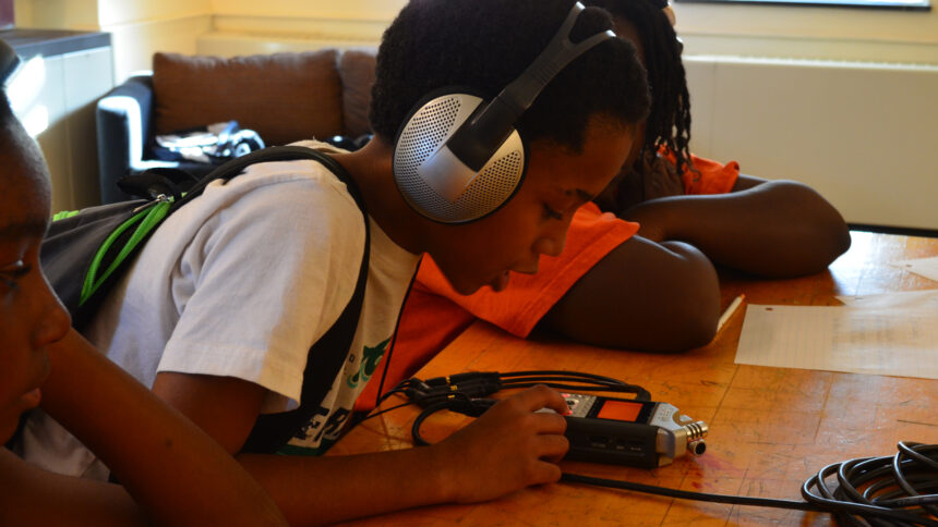 A youth wearing headphones looking at a portable recorder in a classroom