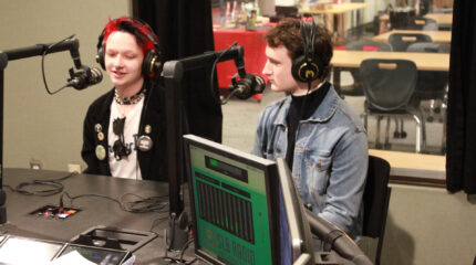 Two teens wearing headphones speaking into microphones in a radio studio