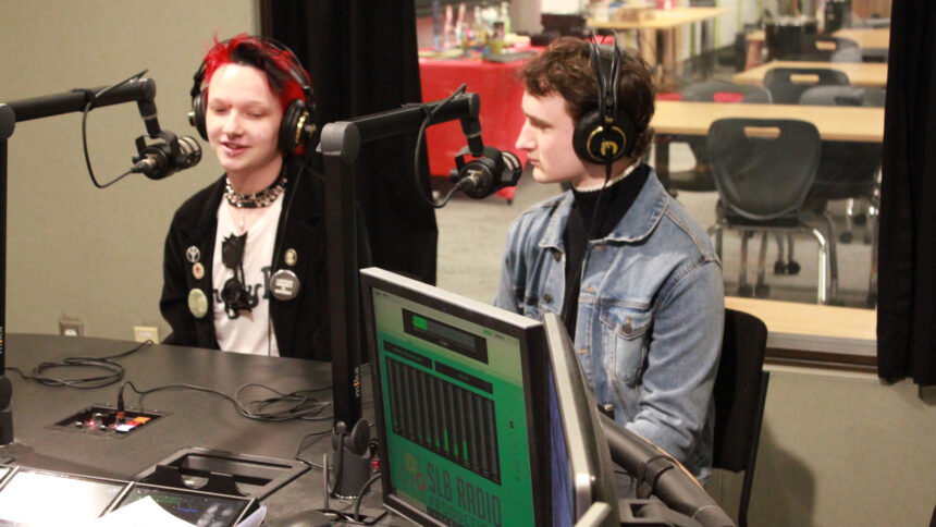 Two teens wearing headphones speaking into microphones in a radio studio