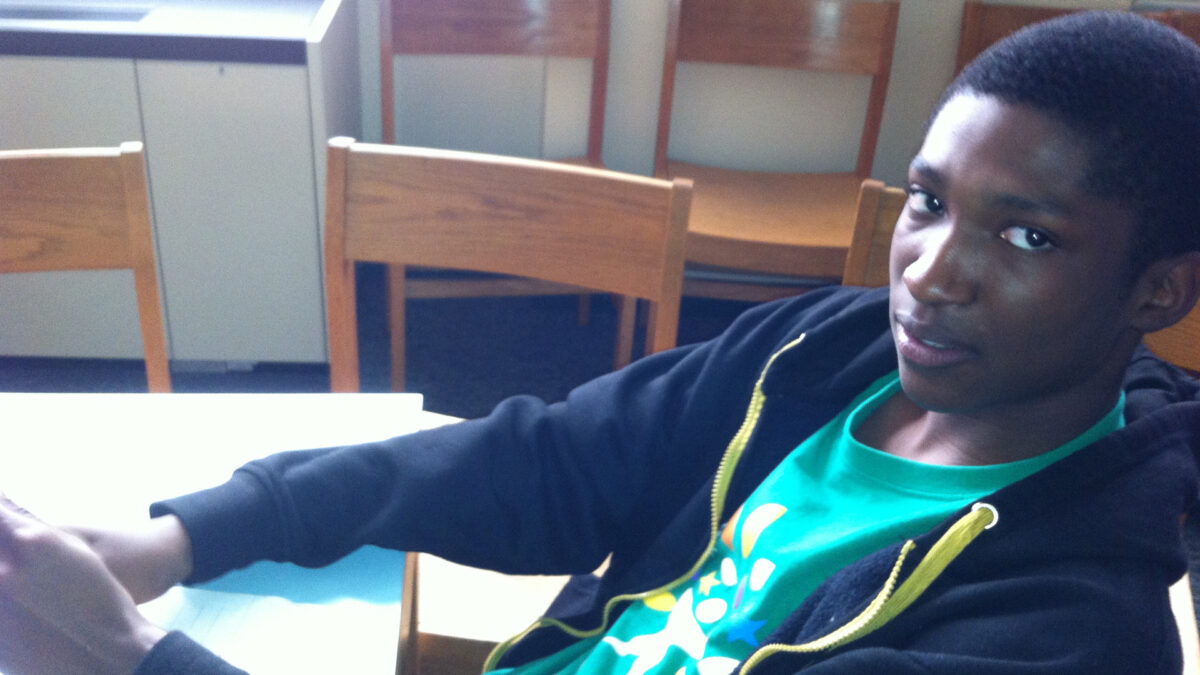 A teen sitting at a table looking at the camera in a library