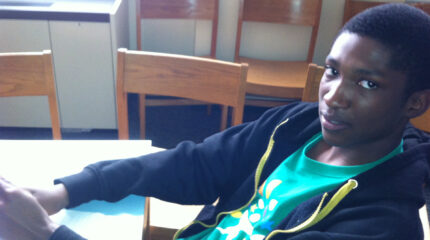 A teen sitting at a table looking at the camera in a library