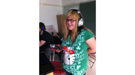 An individual wearing headphones holding a portable recorder in a classroom
