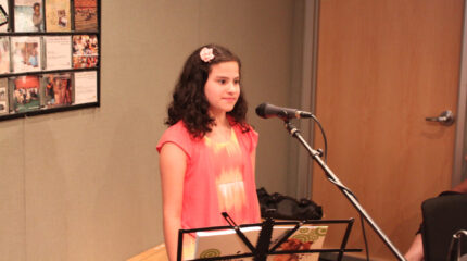 A youth standing behind a microphone and a notebook on a music stand in a radio studio