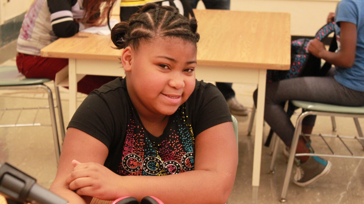 A youth sitting behind a microphone and a pair of headphones at a classroom desk