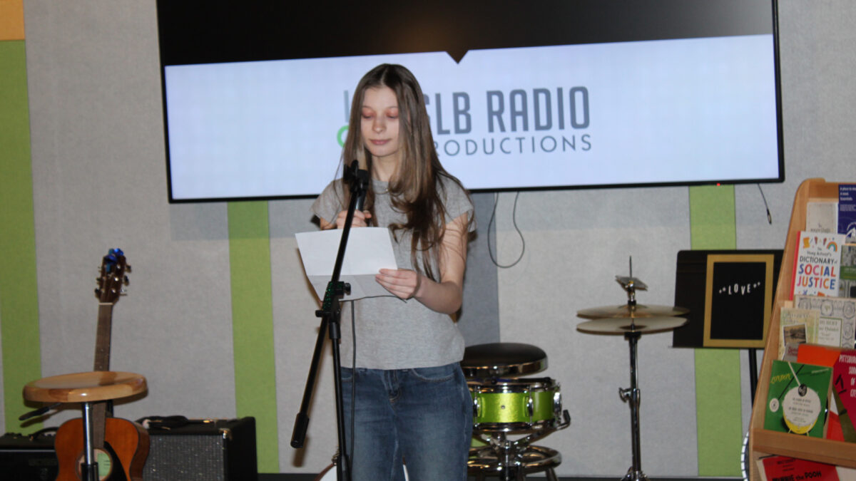 A teen reading a piece of paper into a microphone