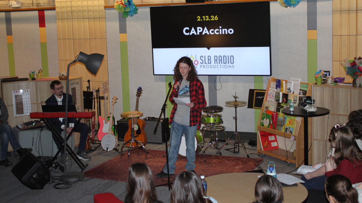 Five teens and an adult listening to a teen reading a piece of paper into a microphone