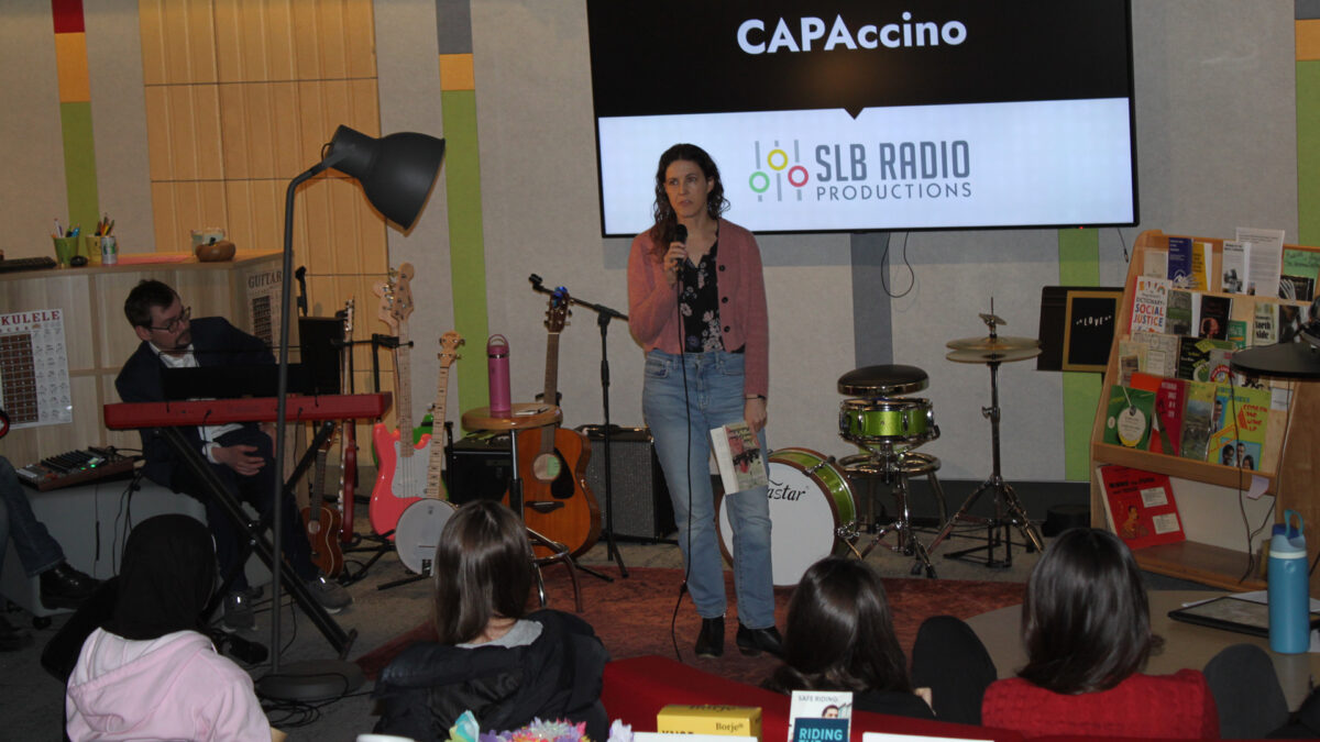 Four teens and an adult listening to another adult speaking into a microphone