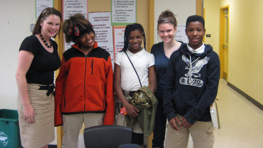 Four teens and one adult smiling and posing in profile in a classroom