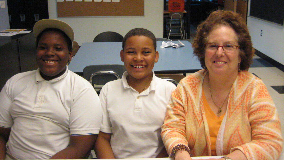 Two youth and an adult smiling at the camera while sitting in a classroom