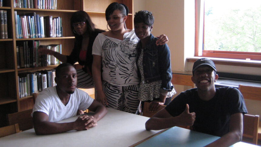 Five teens posing for the camera in a library, one smiling and flashing a thumbs up