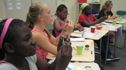 Five youth working with their hands at classroom desks