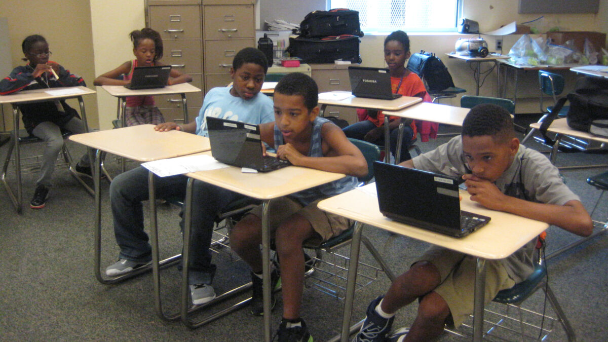 Six youth looking at laptop computers while sitting at classroom desks